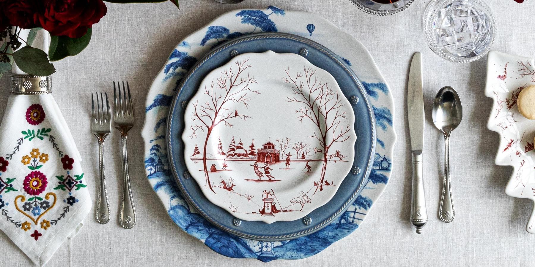 Elegant table setting with decorative plates, silverware, and a floral arrangement on a white tablecloth.