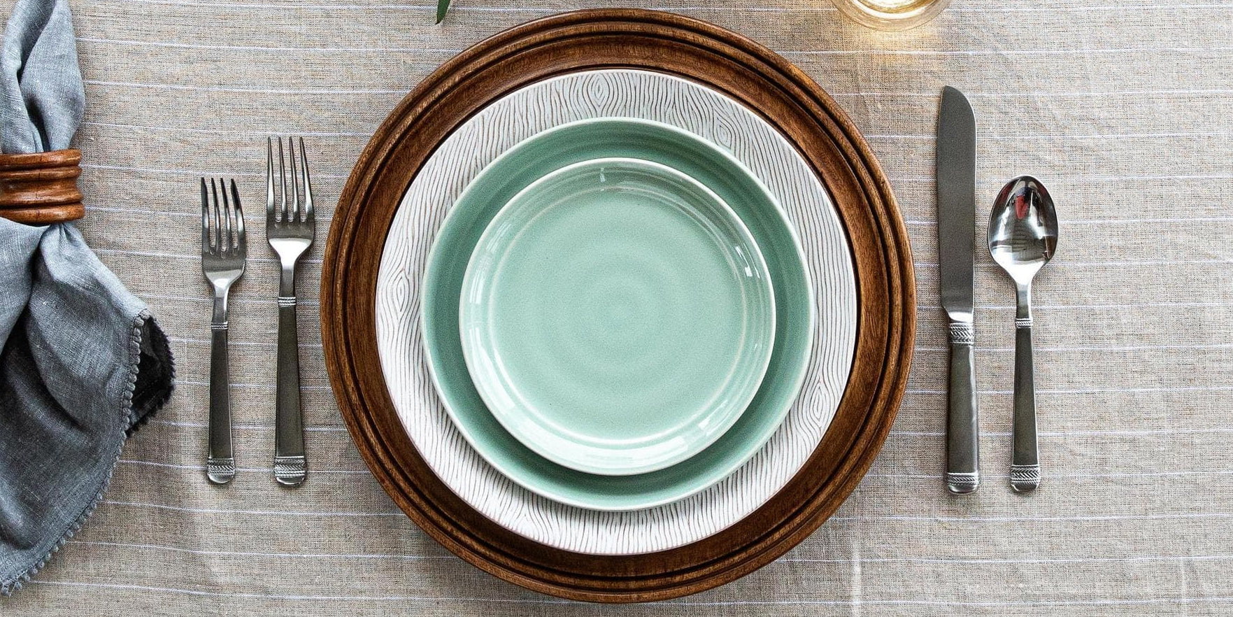 Teal plate on a wooden charger with silverware on a textured tablecloth