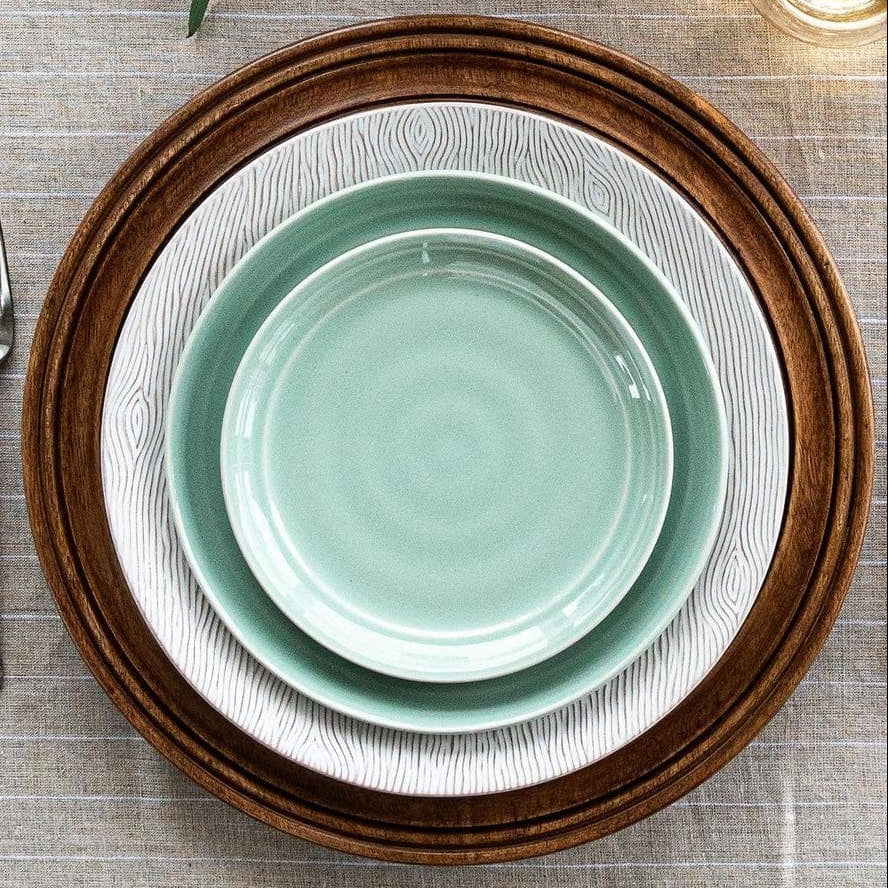 Set of ceramic plates with a wooden charger on a textured surface