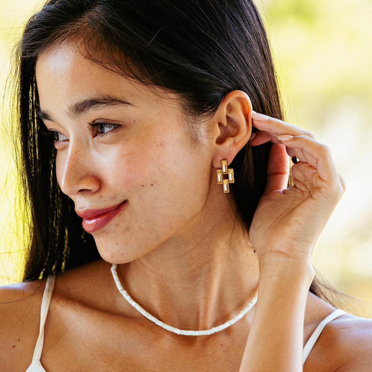 Woman wearing a gold earring outdoors with a blurred natural background