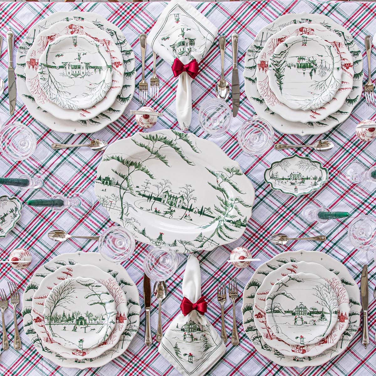 Dining table setting with Christmas-themed plates, napkins, and cutlery on a plaid tablecloth.