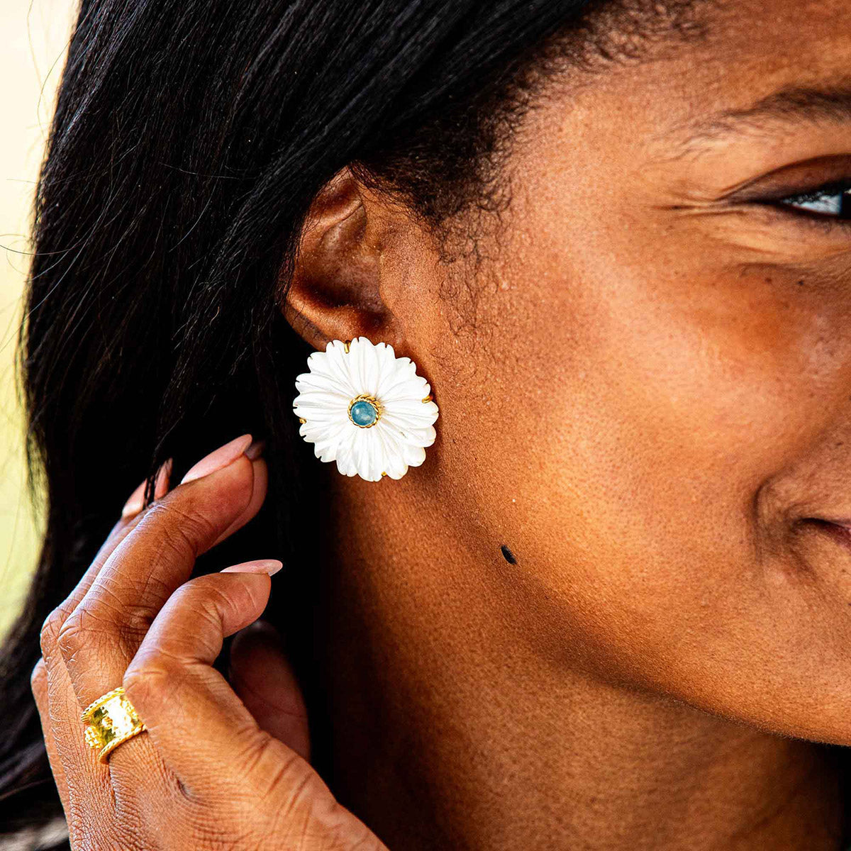 Close-up of a woman wearing a white flower-shaped earring with a blue gemstone.