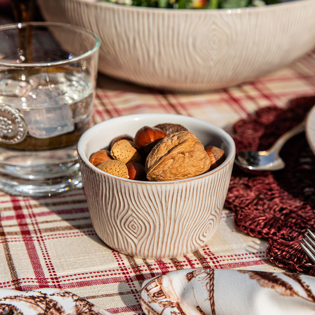 Small ceramic bowl with nuts on a plaid tablecloth with a glass of water and salad in the background.