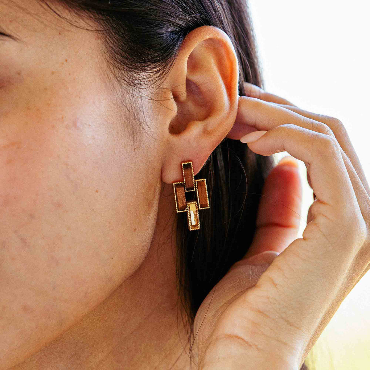 Close-up of an ear wearing a gold geometric earring with a blurred background