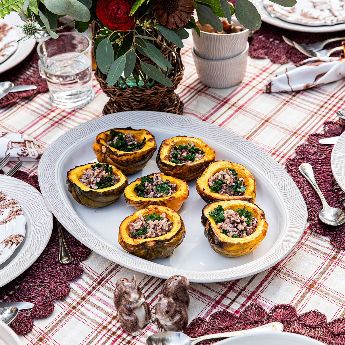 Stuffed acorn squash on a white plate with a festive table setting.