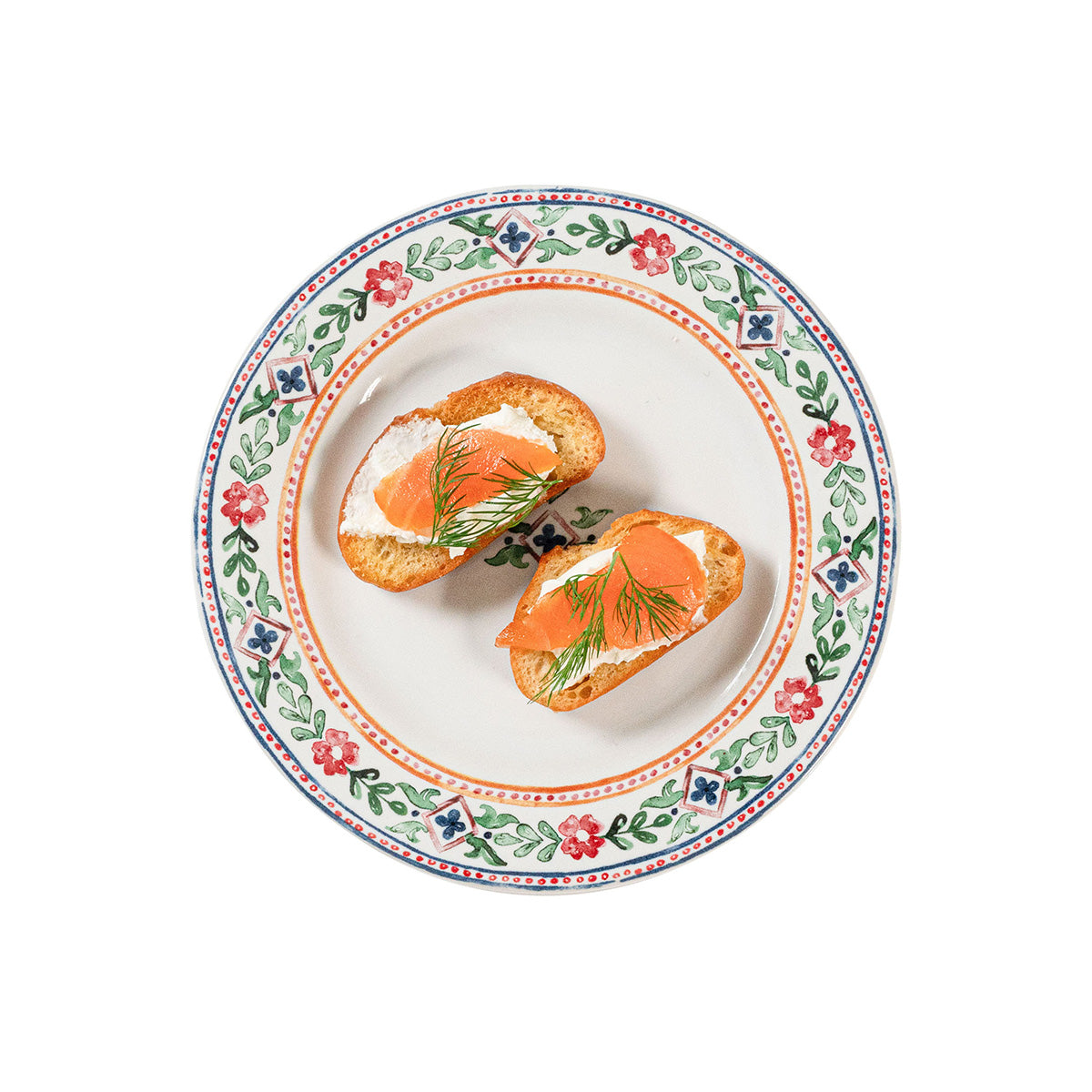 Two crostini with salmon and dill on a decorative plate with floral patterns.