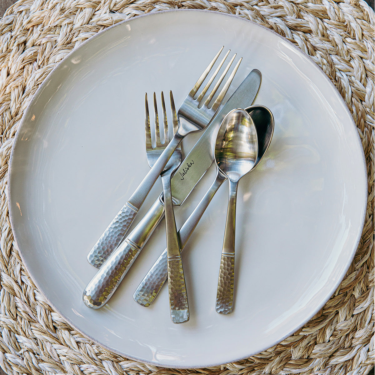 Silver cutlery set on a white plate with woven placemat