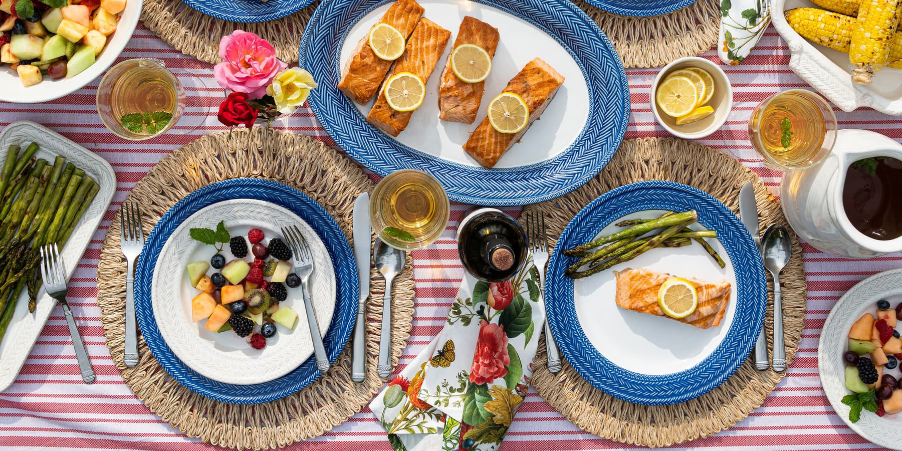 Dinner table set with plates of food, including salmon and vegetables, on a striped tablecloth.