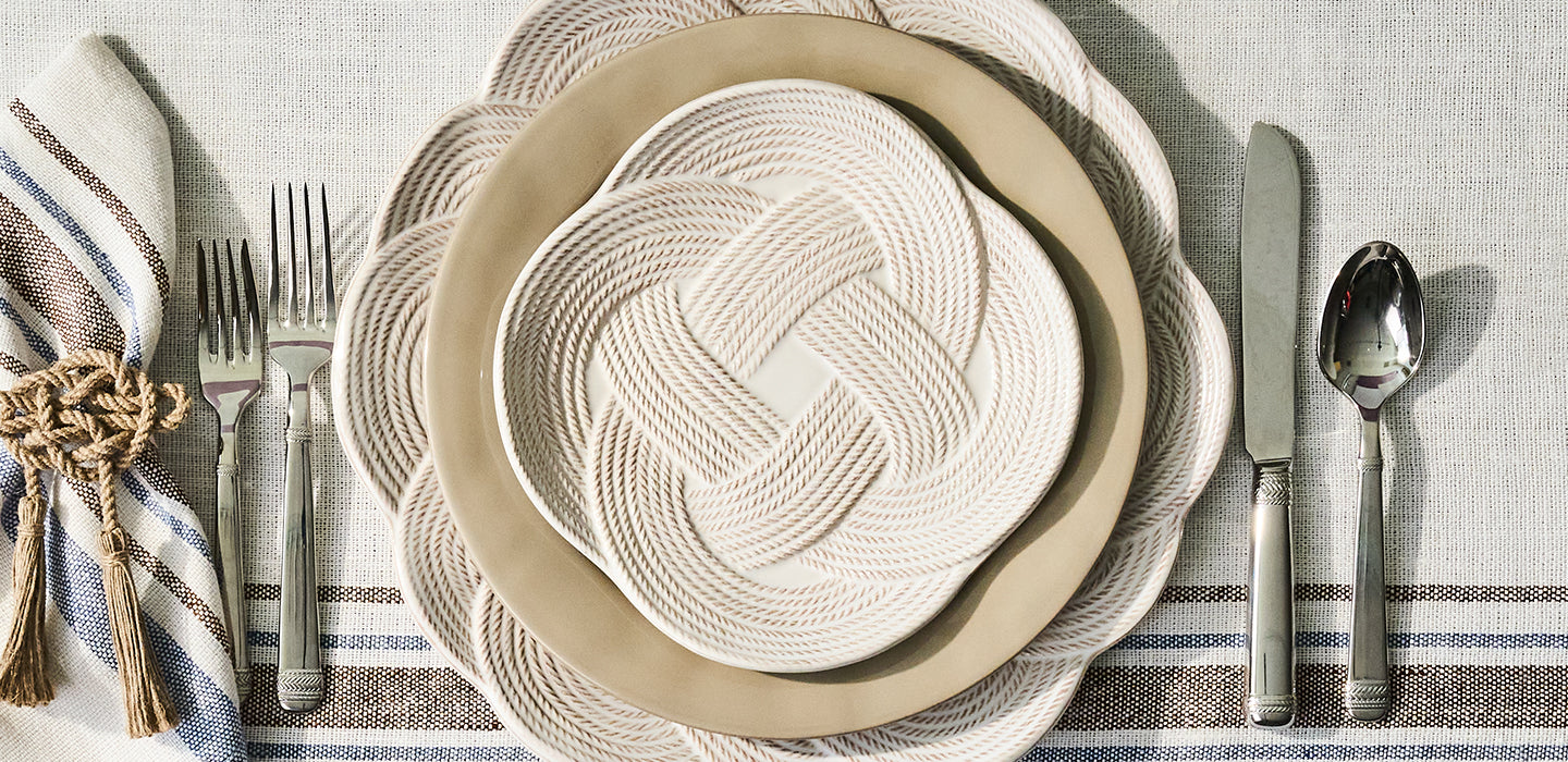Set table with woven plates, silverware, and striped napkin on a gray checkered tablecloth.