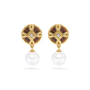 A pair of gold and brown drop earrings with a circular knotwork design, a small clear stone in the center, and a dangling white pearl below, shown on a white background.
