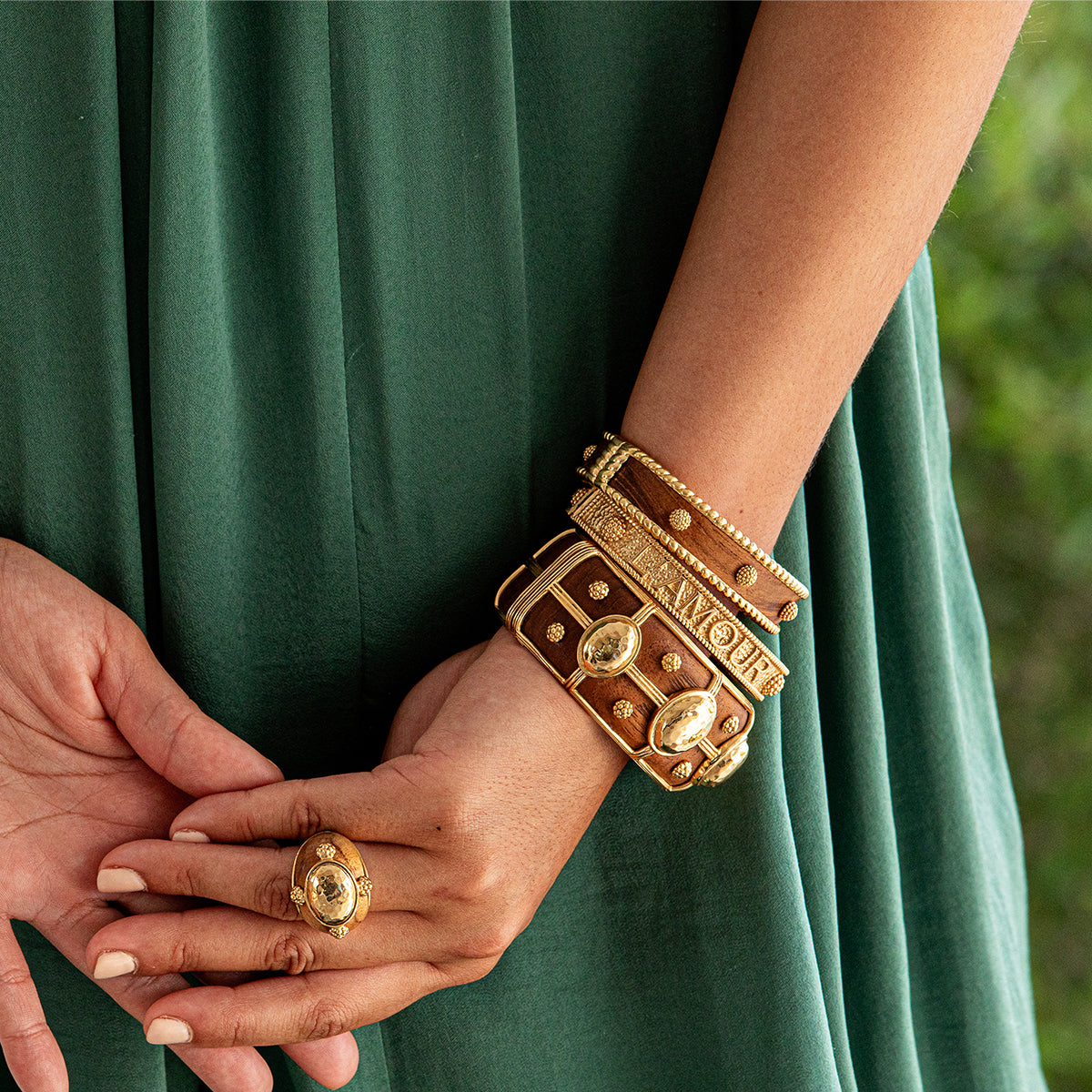 Close-up of hands wearing gold jewelry with a green fabric background