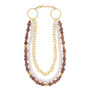 A multi-strand necklace featuring white faux pearls, brown wooden beads, and gold-tone chain links and circular ring connectors, displayed on a solid white background.