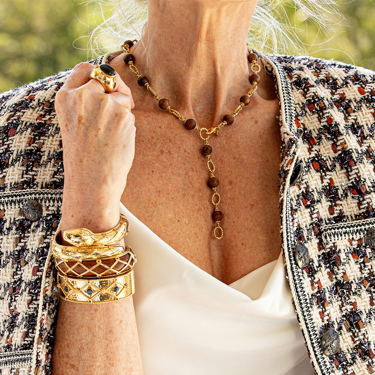 Close-up of a person wearing gold jewelry including a necklace, ring, and bracelets.