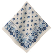 A square cream-colored napkin with a blue floral pattern and a dotted border, displayed diagonally on a white background.