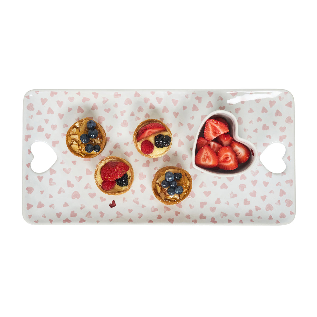 Decorative plate with heart-shaped compartments filled with small tartlets and berries on a white background.